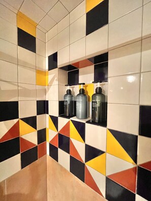 Un baño con un patrón geométrico de azulejos y tres artículos de aseo en un estante.