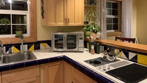 Una cocina con armarios de madera, un tostador, un lavamanos y una ventana con cortinas.