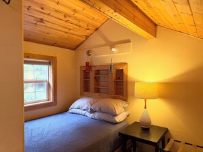Un dormitorio con cama, ventana, mesita de noche con lámpara y estantes de madera.