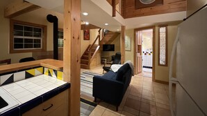 Un interior acogedor con una escalera de madera, una zona de comedor con mesa y sillas, un sofá y una cocina.