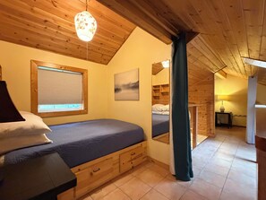 A cozy bedroom with a bed, a window with blinds, a painting, and a wooden ceiling.