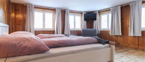 Una camera da letto con un letto, pareti in legno, due finestre con tende, una TV a schermo piatto montata a parete e un pavimento in legno.