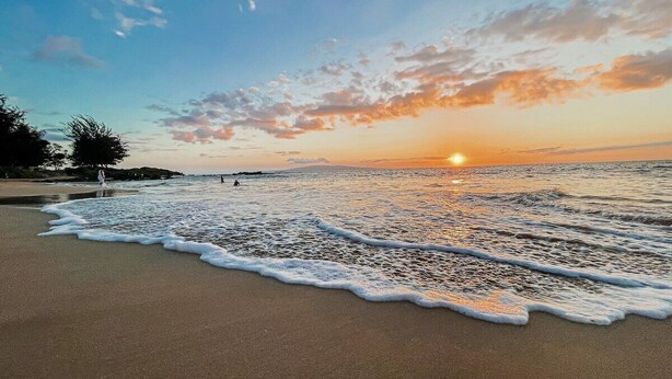 Ein Strand mit Wellen, einem Sonnenuntergang und einem klaren Himmel.