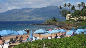 Ein Strand mit Sonnenschirmen, Liegestühlen und Blick auf Berge im Hintergrund.