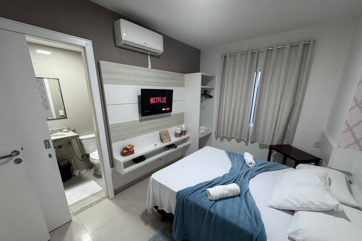 Moderni hotellihuone, jossa on sänky, televisio, jossa näkyy Netflix, kylpyhuone ja ikkuna, jossa on verhot.