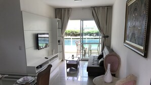 Un salon moderne doté d’un téléviseur à écran plat, d’un canapé, d’une table  à manger et d’un balcon offrant une vue sur la mer.