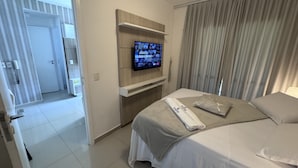 Une chambre d’hôtel avec un lit, un téléviseur fixé au mur, une fenêtre avec des rideaux et une porte donnant sur une autre pièce.