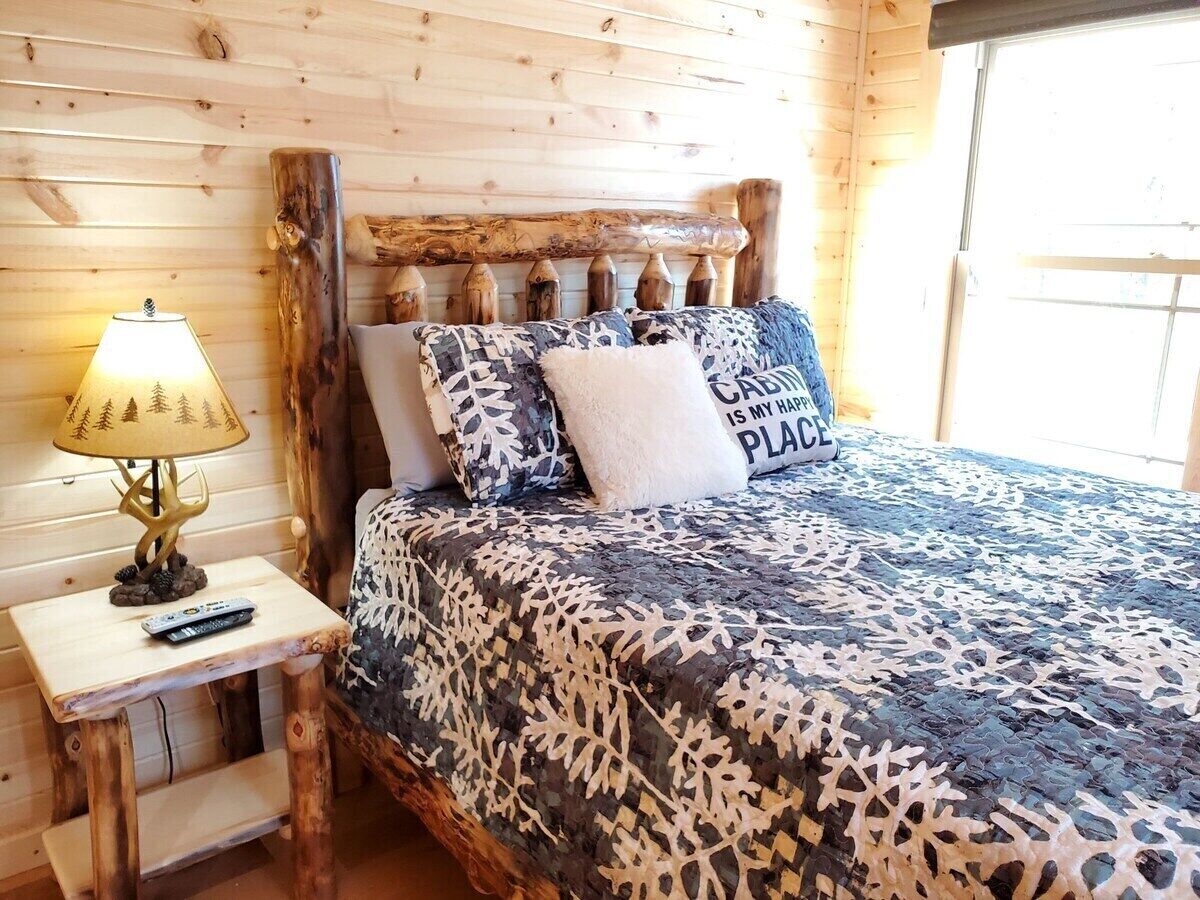 A wooden cabin-style bedroom with a bed, a nightstand with a lamp, and a window.