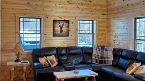 L'intérieur d'une cabane en rondins, avec un canapé en cuir noir, une table basse en bois et une décoration murale représentant une tête de cerf.
