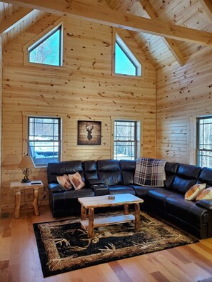 L'intérieur d'une cabane en rondins, avec un canapé en cuir noir, une table basse en bois et une décoration murale représentant une tête de cerf.