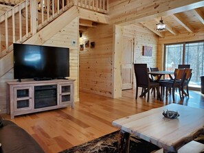 Un intérieur en bois avec un téléviseur posé sur un meuble, un coin repas et un escalier.