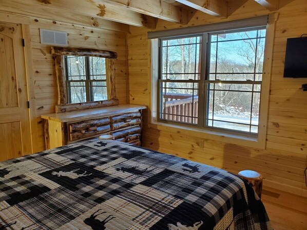 Une chambre à coucher située dans un chalet en rondins, avec un grand lit, une commode et une fenêtre donnant sur la forêt.