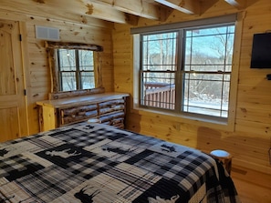 Une chambre à coucher située dans un chalet en rondins, avec un grand lit, une commode et une fenêtre donnant sur la forêt.