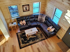 Un interior de cabaña acogedor con un sofá seccional de cuero negro, una mesa de centro de madera y una alfombra rústica.