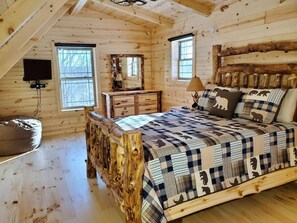 A log cabin bedroom with a bed, dresser, and a large mirror.