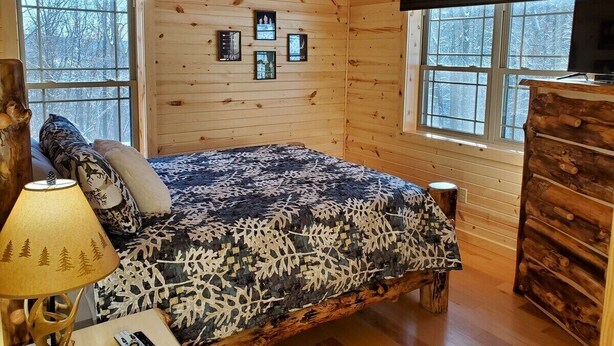 Une chambre confortable dans un chalet en rondins, avec un lit, une commode et une fenêtre donnant sur la forêt.