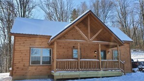 Une cabane en bois avec un porche, une fenêtre et un toit recouvert de neige.