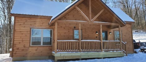 A wooden cabin with a porch, a window, and a snow-covered roof.