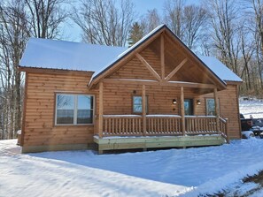 Une cabane en bois avec un porche, une fenêtre et un toit recouvert de neige.