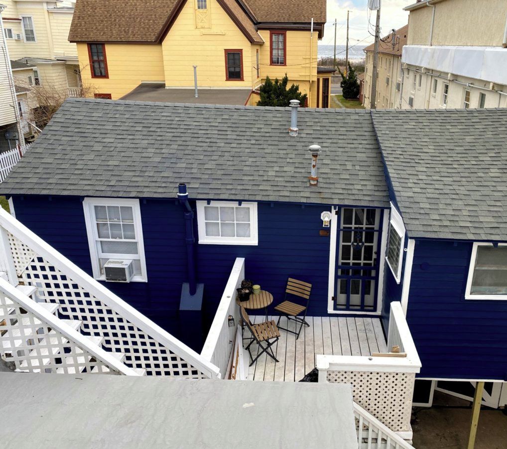 A two-story house with a blue exterior, a deck with a table and chairs, and a small window.