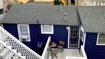 A two-story house with a blue exterior, a deck with a table and chairs, and a small window.