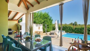 An outdoor dining area with a glass table, chairs, and a view of a swimming pool and greenery. - Lovely home in Naselje Muzini with sauna (Naselje Muzini)