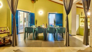 A dining area with a table set for six, blue shutters on the windows, and a cart with bottles. - Lovely home in Naselje Muzini with sauna (Naselje Muzini)
