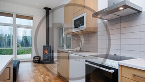 Een moderne keuken met een houtgestookte kachel, een inbouwoven en een groot raam met uitzicht op een bos.