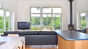 Een moderne woonkamer met een leren bank, een flatscreen televisie en een groot raam met uitzicht op een bebost gebied.