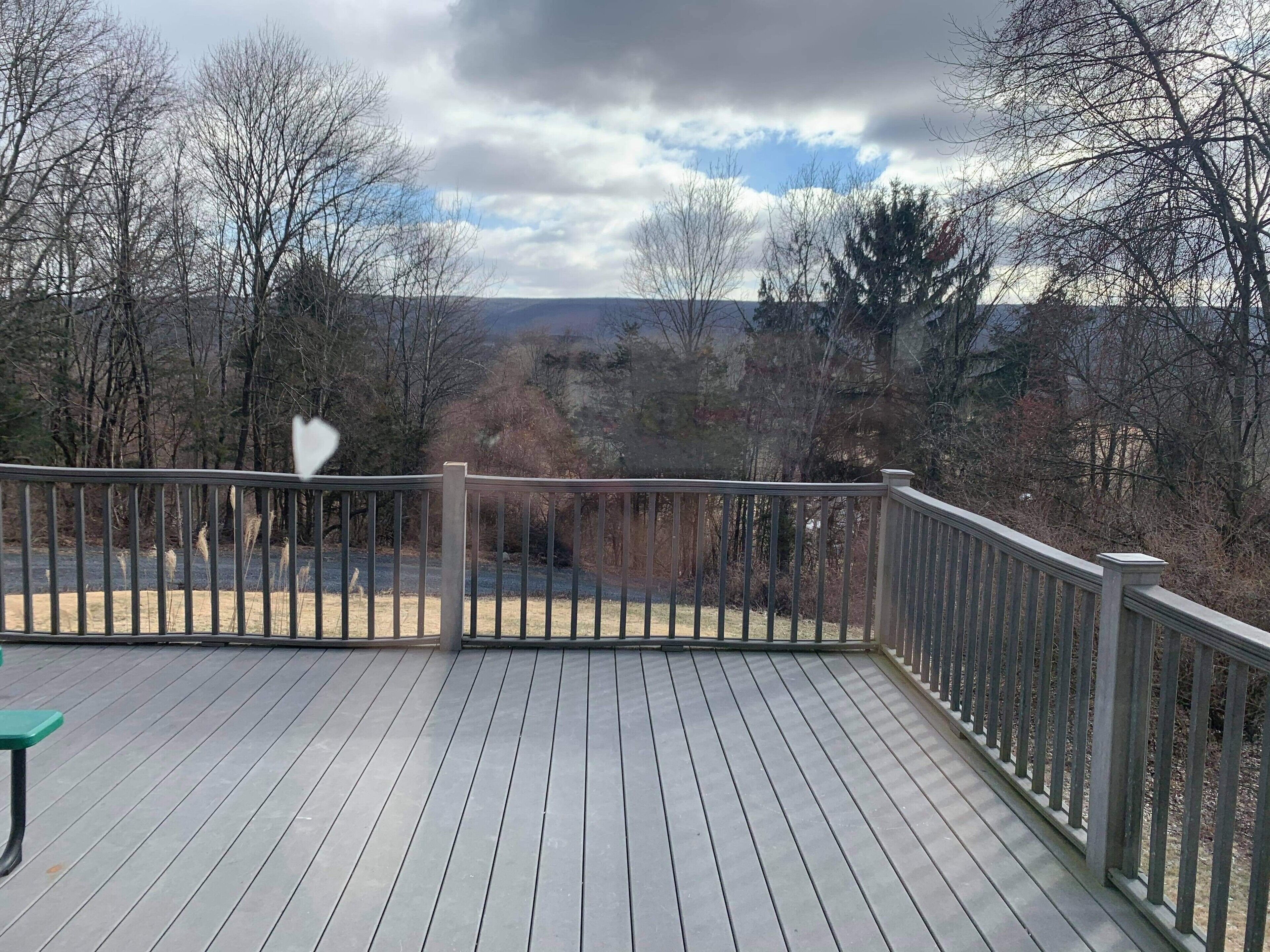 A wooden deck with a metal railing, overlooking a landscape with trees and hills.