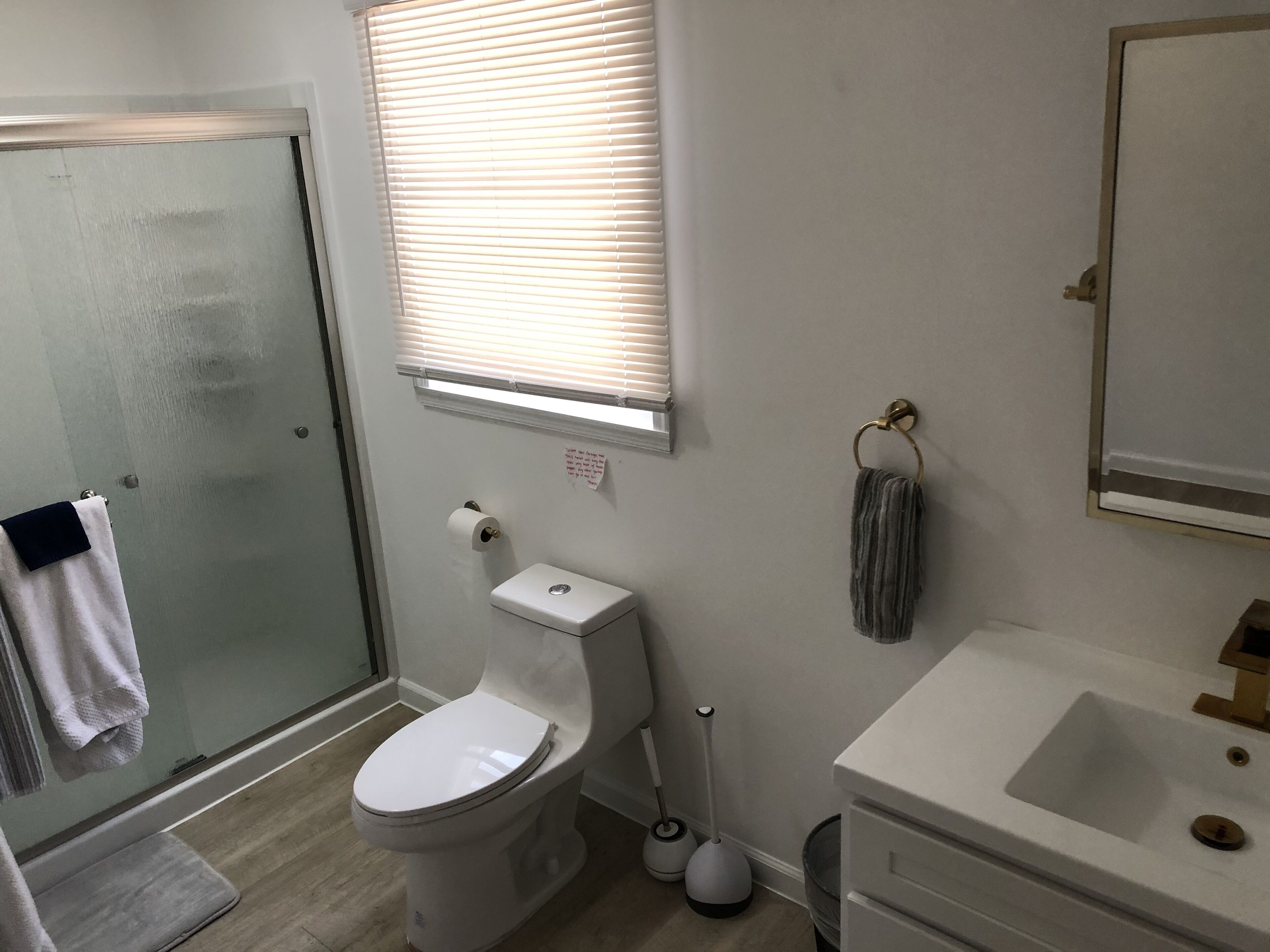 A bathroom with a toilet, a sink, a shower, and a window with blinds.