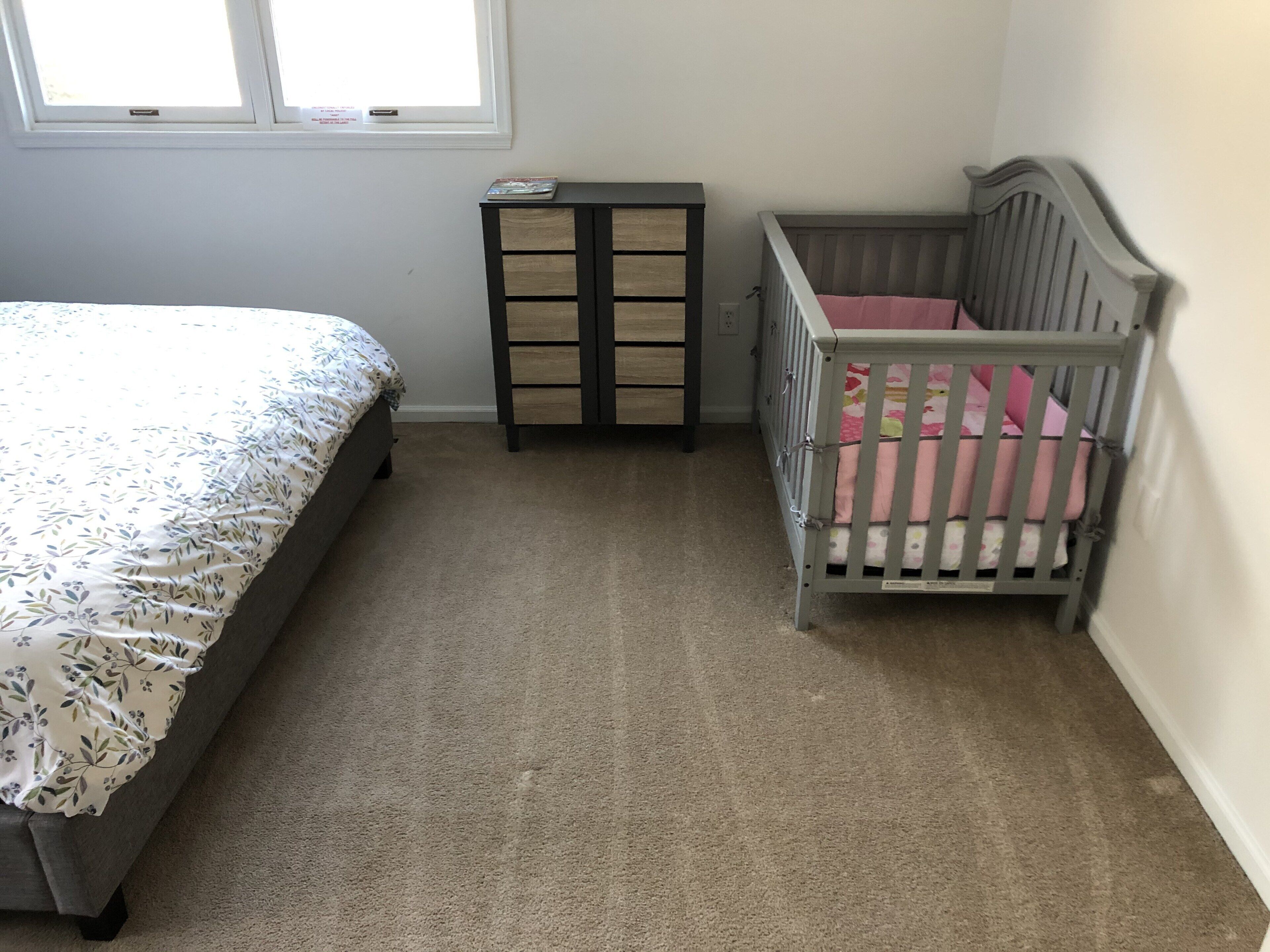 Un dormitorio con una cama, una cuna, un tocador pequeño y una ventana.