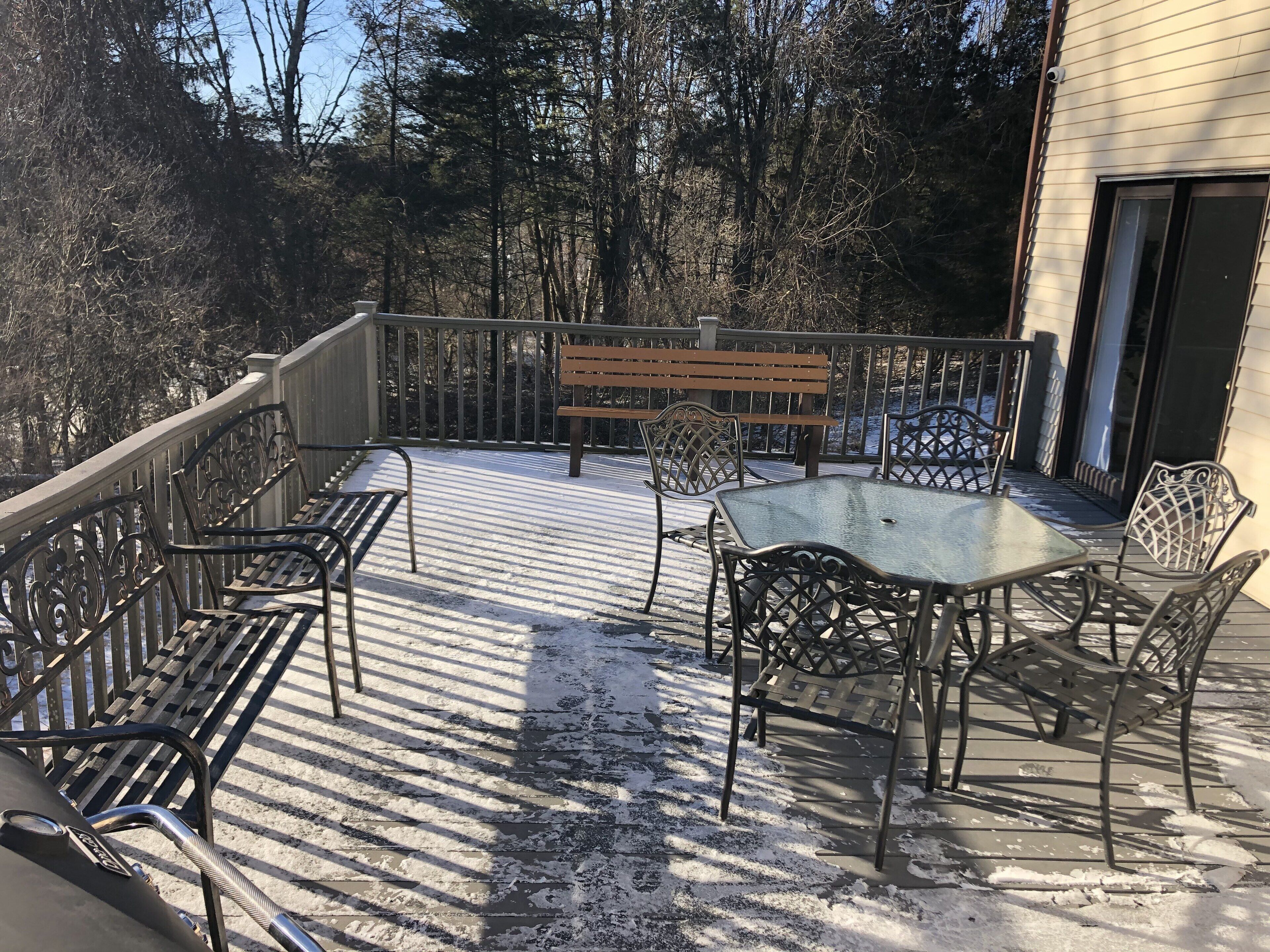 A covered outdoor deck with metal railings, a wooden bench, and metal chairs.