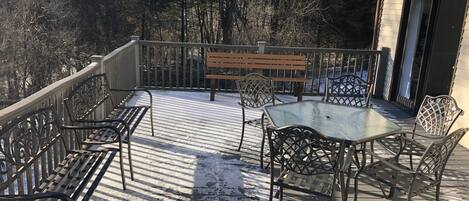 Una terraza techada al aire libre con barandillas de metal, un banco de madera y sillas de metal.