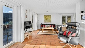 Un salon spacieux comprenant un canapé, une table basse et un téléviseur. Une porte-fenêtre coulissante donne accès à un espace extérieur.