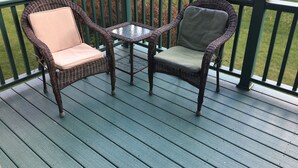 A deck with two wicker chairs and a glass table.