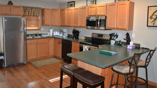 A modern kitchen with wooden cabinets, stainless steel appliances, and a bar area with stools.