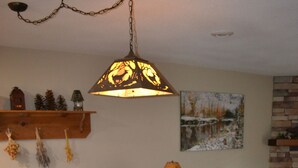 A dining area with a wooden table and floral upholstered chairs, a hanging lamp, and a painting on the wall.