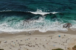 A beach with waves crashing onto the shore, people relaxing, and a few umbrellas.