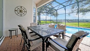 Un patio con una mesa y sillas, un adorno de pared con forma de brújula, y vistas a una piscina y follaje.