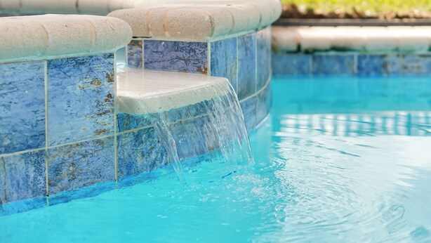 Una piscina con una cascada integrada y un borde de azulejos.
