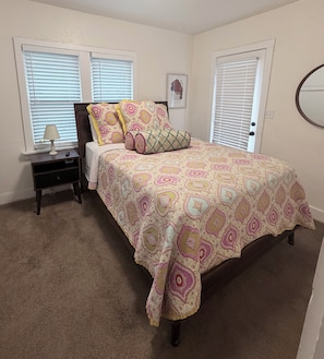 A bedroom with a bed, nightstand, lamp, and two windows with blinds. - Renovated Casa Verde, in the heart of OKC (Oklahoma City)