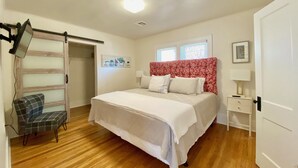 Un dormitorio con una cama, una silla, una mesita de noche, una lámpara, una luz en el techo y una ventana.