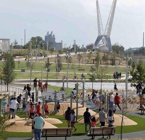 Un parque público con áreas de juegos, bancos y una noria grande al fondo.