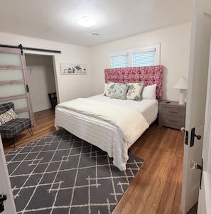 A bedroom with a bed, a chair, a nightstand, a lamp, and a window with blinds. - Renovated Casa Verde, in the heart of OKC (Oklahoma City)