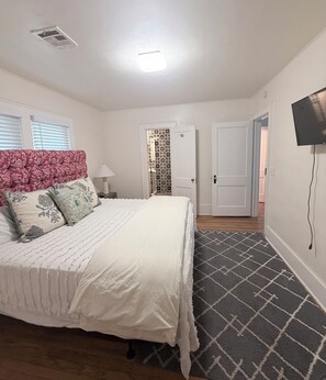 A bedroom with a bed, a nightstand, a lamp, a TV, and a patterned rug. - Renovated Casa Verde, in the heart of OKC (Oklahoma City)