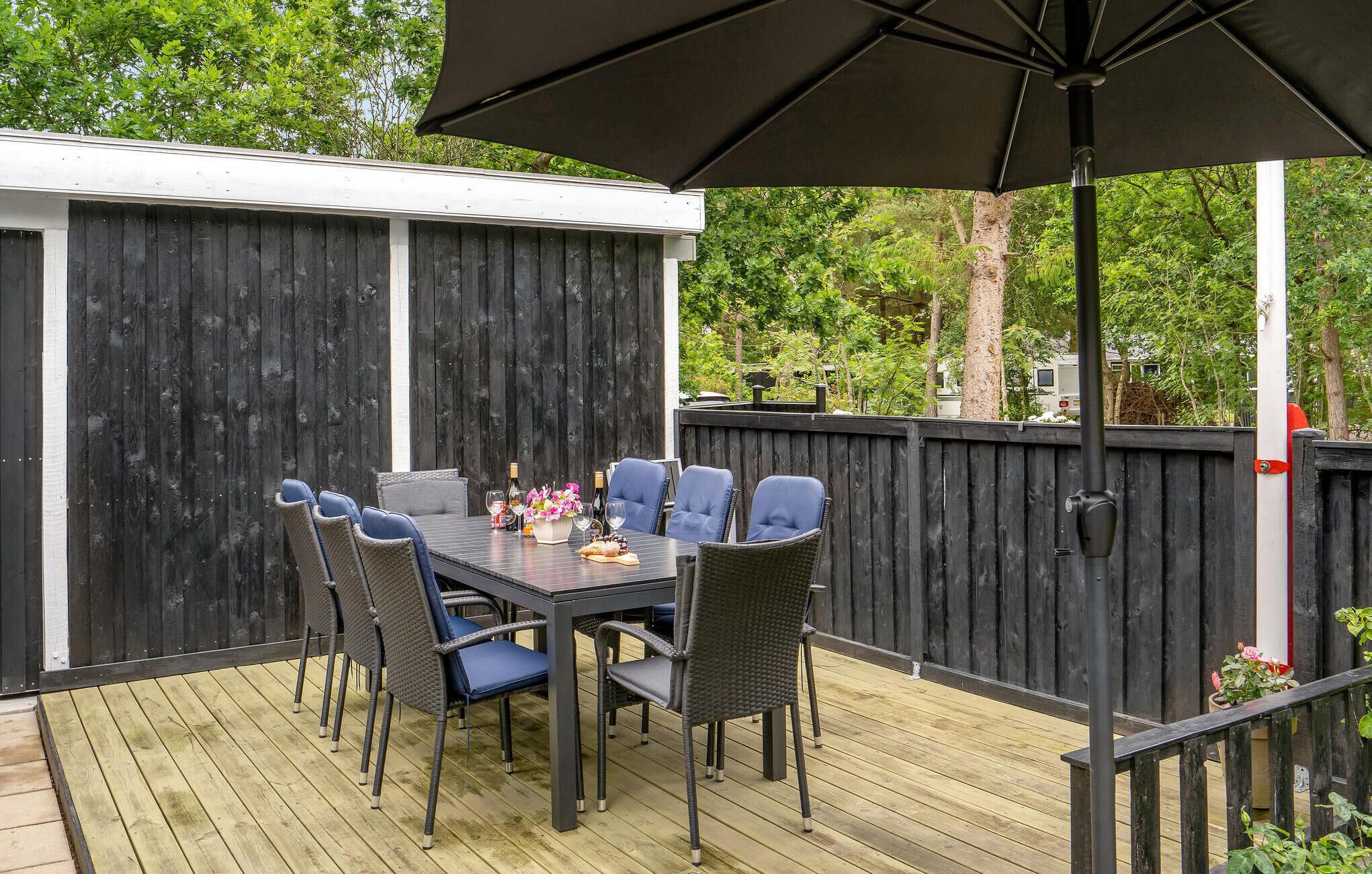 An outdoor patio with a table set for dining, surrounded by chairs, under a large umbrella.