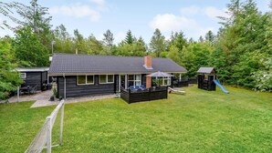 Ein Haus mit überdachter Terrasse, einem Spielbereich mit Rutsche und einem umzäunten Garten.