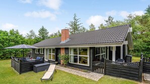Ein Haus mit überdachter Terrasse, Liegestuhl und kleinem Garten.