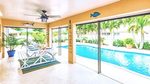 Un espace aménagé au bord de la piscine, doté d’un ventilateur de plafond, d’une table avec des chaises et offrant une vue sur la piscine.
